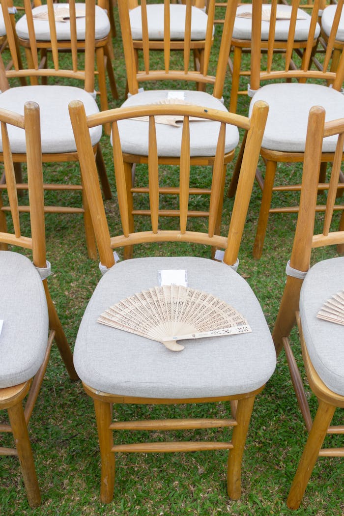 Elegant outdoor wedding setting with wooden chairs and decorative hand fans.